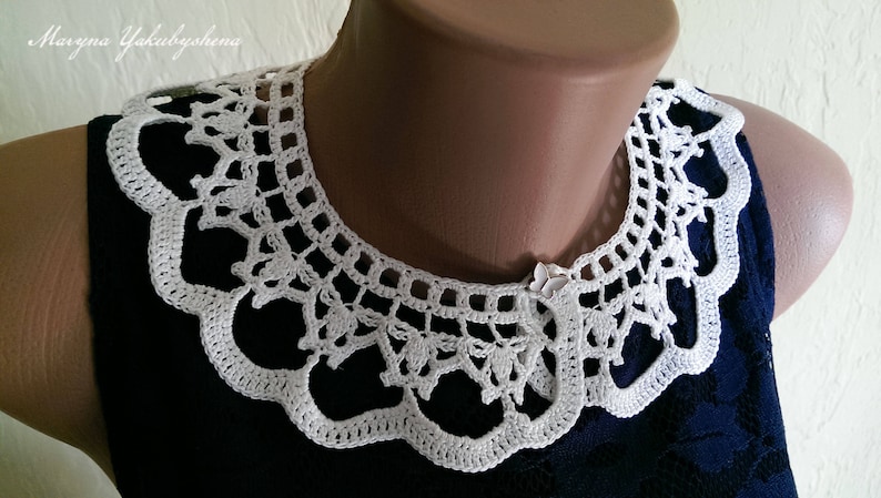 Puede incluir: Cuello blanco de ganchillo con borde festoneado y un intrincado dise&ntilde;o calado. El cuello se muestra sobre un maniqu&iacute; y se coloca sobre un vestido azul oscuro. Un delicado accesorio hecho a mano.