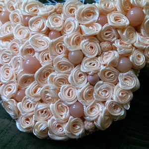 May include: A peach-colored heart-shaped brooch made of fabric roses and pearl-like beads.