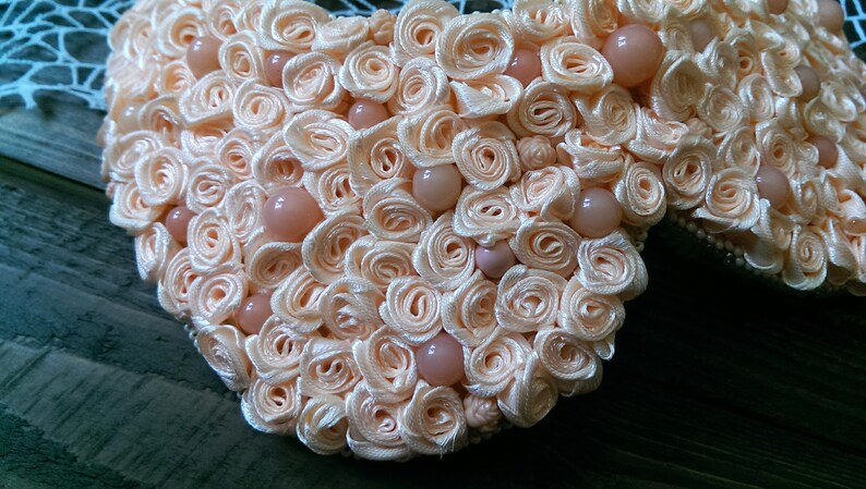 May include: A peach-colored heart-shaped brooch made of fabric roses and pearl-like beads.