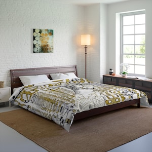 May include: A white and gold duvet cover with a geometric pattern. The duvet cover is on a bed with white pillows and a brown headboard. The bed is in a bedroom with a white brick wall, a window, and a lamp.