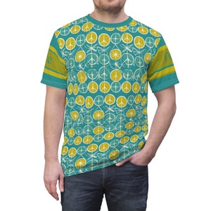 May include: A teal blue t-shirt with a pattern of yellow peace signs and white dragonfly designs. The shirt has yellow and blue stripes on the sleeves and the word "Peace" on the right sleeve.