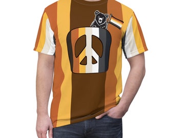 May include: A short-sleeved t-shirt with a striped pattern in shades of brown, orange, and yellow. A peace sign is centred on the shirt, with a bear holding a pride flag inside the peace sign.