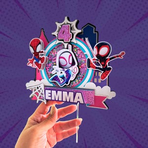 May include: A colorful cake topper featuring Spider-Man characters and the name "EMMA". The design includes a number "4" and a cityscape silhouette. The topper is held by a clear plastic stick, perfect for a birthday cake.