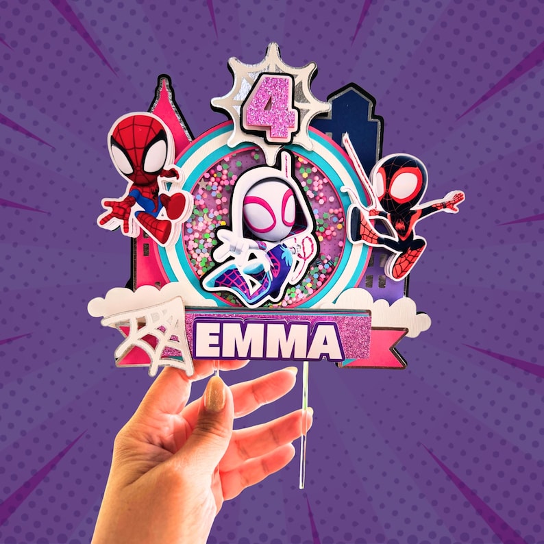May include: A colorful cake topper featuring Spider-Man characters. The design includes a central bubble with confetti, the number 4, and the name "EMMA". The background is a purple comic book style.