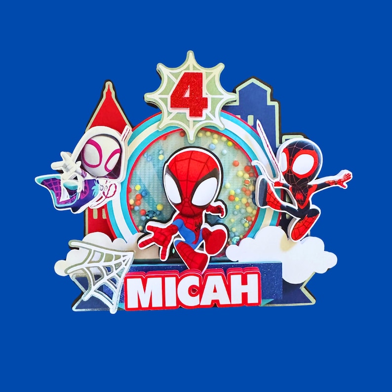 May include: A colorful cake topper featuring Spider-Man and other characters. The number "4" is displayed, along with the name "MICAH". The design includes a cityscape and a web, all set against a blue background.
