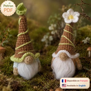 Peut inclure: Deux gnomes au crochet avec de hauts chapeaux pointus marron entourés de fil vert clair. Le gnome de gauche a une feuille verte sur son chapeau, tandis que celui de droite porte une fleur blanche. Ils ont des nez ronds et des barbes blanches.