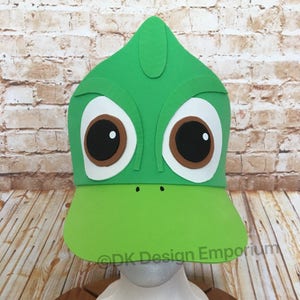 May include: Green felt chameleon hat with large brown eyes and a white felt beak. The hat is on a white mannequin head.  ©DK Design Emporium