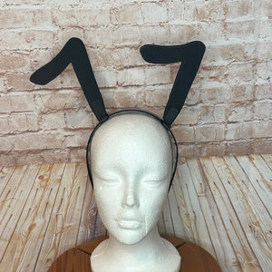 May include: Black bunny ears headband on a white mannequin head. The headband is made of black felt and has two large, floppy ears.