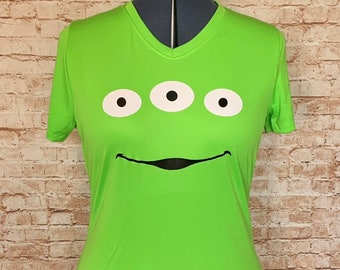 May include: A lime green short-sleeved t-shirt with a black and white alien face graphic. The alien has three eyes and a smiling mouth.