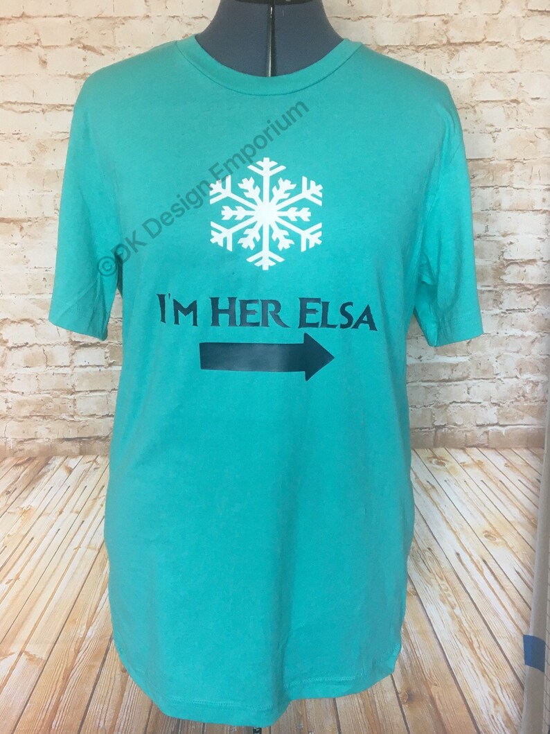 May include: Teal blue t-shirt with a white snowflake and black text that reads "I'm Her Elsa" with a black arrow pointing to the right.