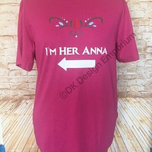 May include: A pink t-shirt with a white arrow pointing to the left and the text "I'm Her Anna" in white. The shirt has a green and blue design above the text. The text "&copy;DK Design Emporium" is in the bottom right corner.