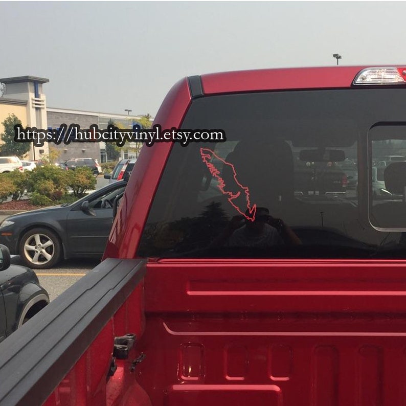 May include: A red pickup truck with a black window and a red outline of the province of British Columbia on the back window. The truck is parked in a parking lot. The text "https://hubcityvinyl.etsy.com" is visible on the truck.
