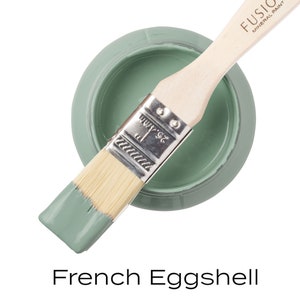 May include: A round container of French Eggshell mineral paint with a wooden paintbrush. The paintbrush is dipped in the pale green paint. The text "FUSION MINERAL PAINT" is printed on the paintbrush handle. The text "French Eggshell" is printed below the paint container.
