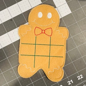 Könnte beinhalten: Ein Lebkuchenmann-Filz-Anhänger mit roter Schleife und grünen und weißen Nähten.