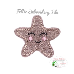 May include: A pink and brown felt star with a smiling face and eyelashes. The star is embroidered with a glittery texture. The text "Precut Felties SVG File Example for Felties" is visible in the image.