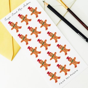 May include: A sheet of gingerbread man stickers with red hats and green scarves, next to a yellow envelope, a pencil, and a paintbrush. The text on the sticker sheet reads "Ginger Bread Man Stickers" and "Pear Tea Paperie."
