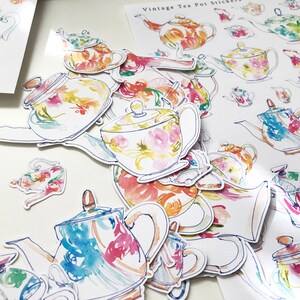 May include: A set of vintage tea pot stickers featuring watercolor illustrations of teapots with floral patterns in shades of pink, blue, yellow, and green. The stickers are perfect for adding a touch of vintage charm to your home decor.