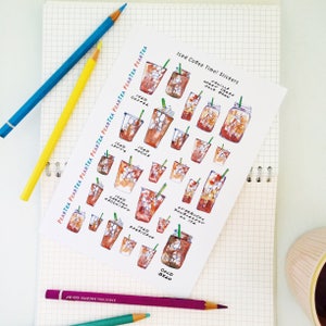 May include: A sheet of stickers featuring various iced coffee drinks, including iced coffee, iced latte, iced mocha, iced caramel macchiato, iced americano, Starbucks Doubleshot on Ice, vanilla sweet cream cold brew, and cold brew. The stickers are illustrated in a watercolor style with brown, white, and green colors.