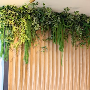 Luxury faux greenery garland with trailing ferns and layered foliage installed above wooden wall panels and blue booth seating in a modern café interior