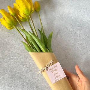 May include: A bouquet of yellow tulips wrapped in brown paper with a tag that reads "happiness blooms from within".