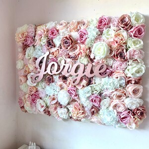 May include: A pink, white and peach floral wall decor with the name "Jorgie" in rose gold lettering.