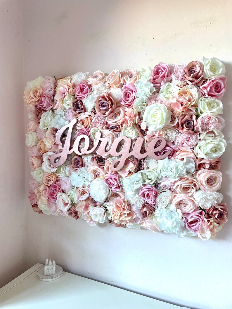 May include: A pink, white and peach floral wall decor with the name "Jorgie" in rose gold lettering.