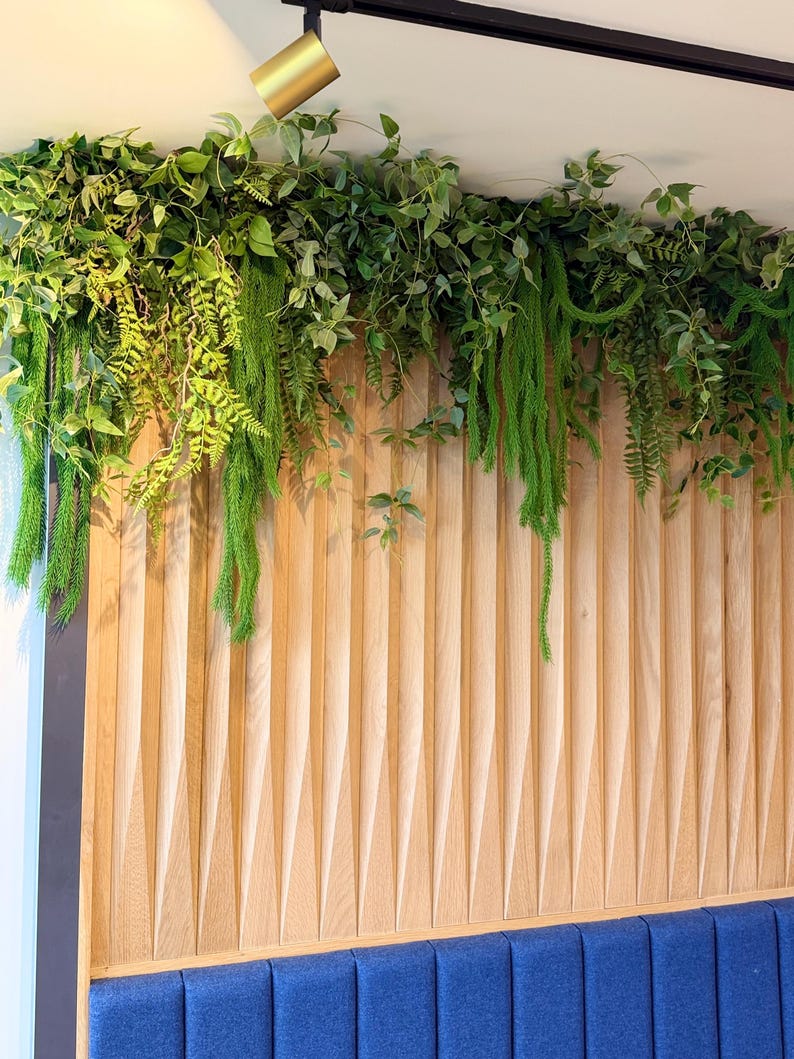Luxury faux greenery garland with trailing ferns and layered foliage installed above wooden wall panels and blue booth seating in a modern café interior