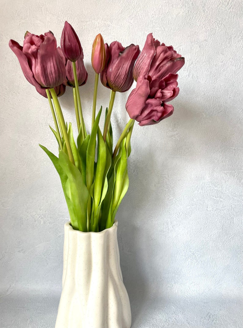 May include: A bouquet of pink tulips with green stems in a white ceramic vase with a textured surface.