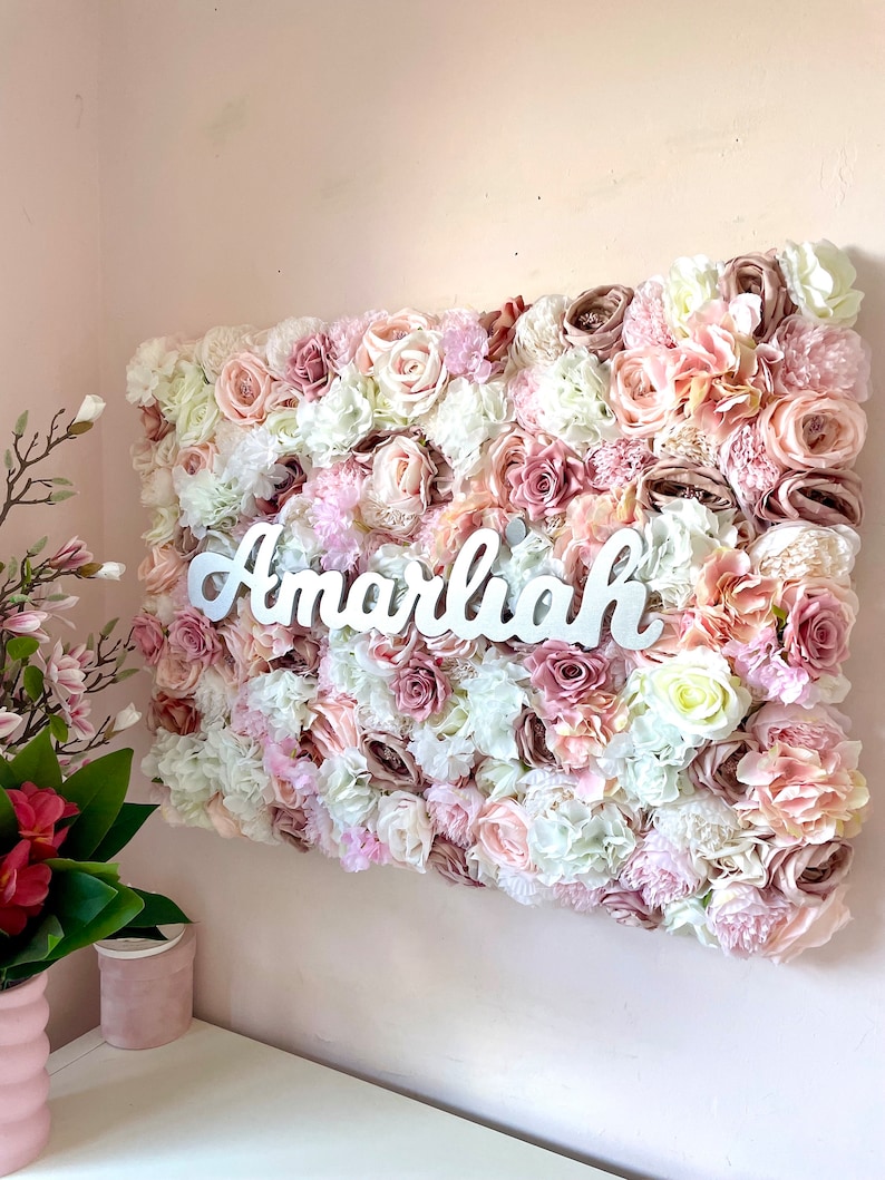 May include: A white floral wall with pink and white flowers, with the name "Amarliah" written in white letters.
