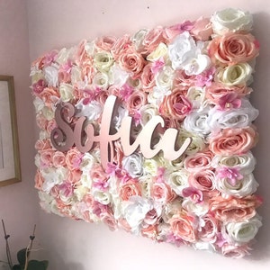 May include: A pink, white and cream floral wall backdrop with the name "Sofia" written in rose gold letters.