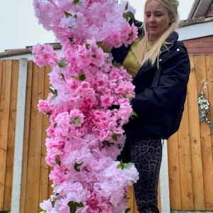May include: A person holding a large bouquet of pink and white artificial cherry blossoms. The flowers are arranged in a cascading style, with the pink blossoms at the top and the white blossoms at the bottom.