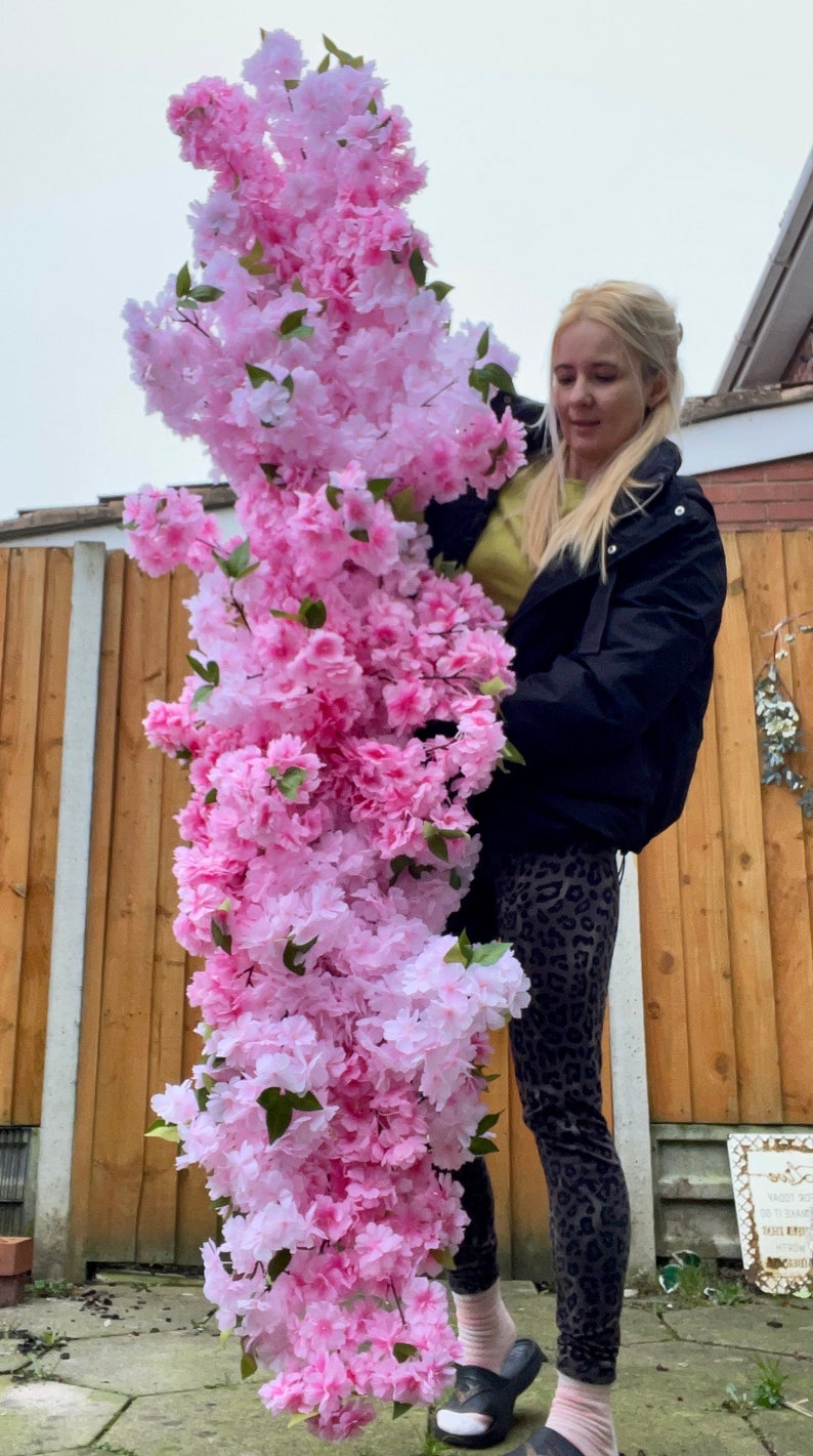 May include: A person holding a large bouquet of pink and white artificial cherry blossoms. The flowers are arranged in a cascading style, with the pink blossoms at the top and the white blossoms at the bottom.