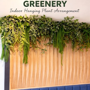 May include: A wall-mounted indoor hanging plant arrangement with lush cascading greenery. The arrangement features various shades of green foliage, including hanging plants. The greenery is above a wooden panel and a blue upholstered bench. Text reads "Lush Cascading Greenery" and "Indoor Hanging Plant Arrangement."