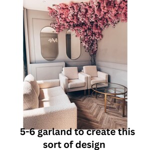 May include: A living room interior with a white couch, two white armchairs, and a gold metal coffee table. The room is decorated with a pink floral garland hanging from the ceiling.