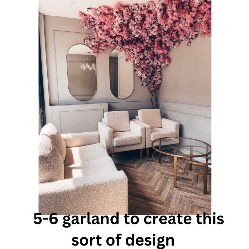 May include: A living room interior with a white couch, two white armchairs, and a gold metal coffee table. The room is decorated with a pink floral garland hanging from the ceiling.