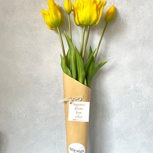 May include: A bouquet of yellow tulips wrapped in brown paper with a tag that reads "happiness blooms from within". The bouquet is tied with twine and has a sticker that says "SDesign Floral".