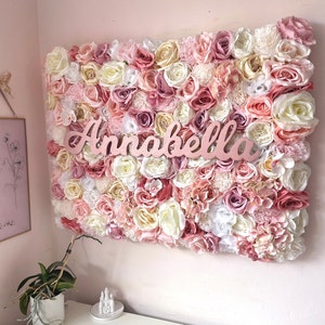 May include: A pink and white flower wall with the name Annabella written in pink letters.