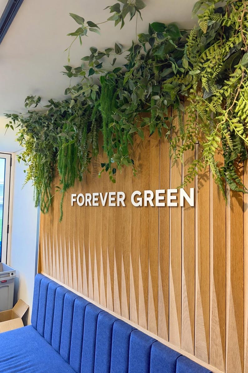 May include: A wooden wall with the words "FOREVER GREEN" in white. The wall has a blue bench below and is decorated with hanging green plants. The wooden panels are vertically aligned.