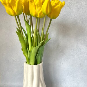 May include: A bouquet of yellow tulips in a white ceramic vase with a textured surface.