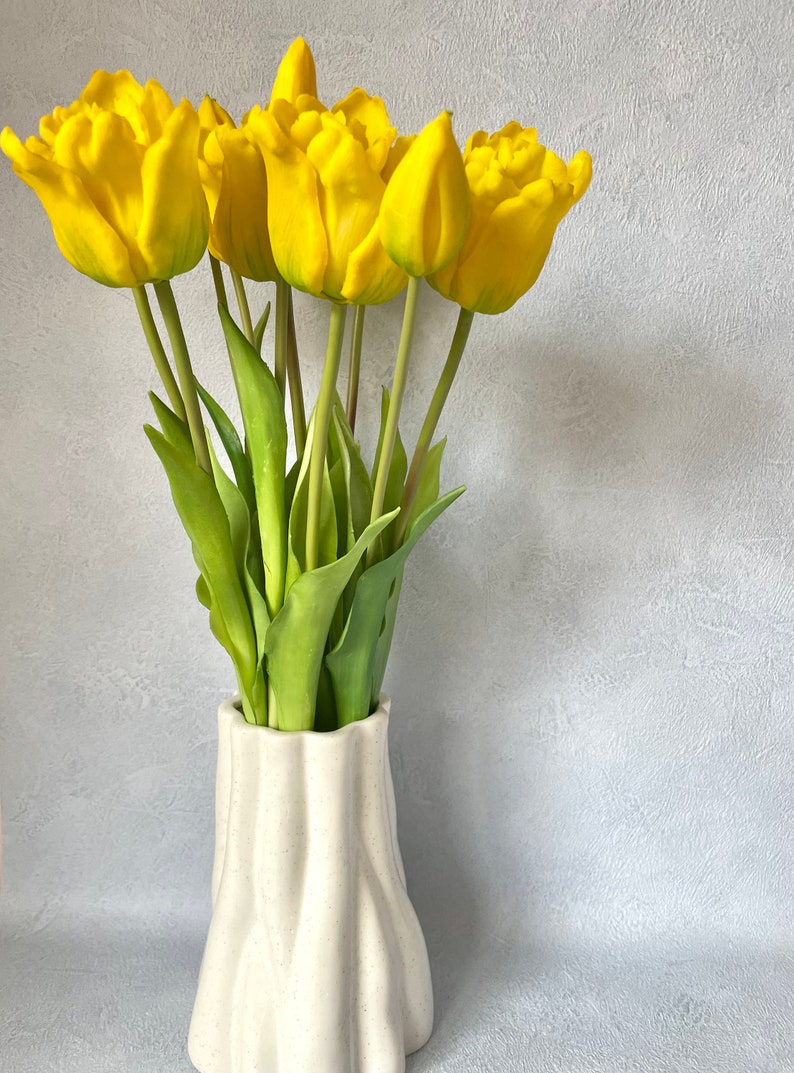 May include: A bouquet of yellow tulips in a white ceramic vase with a textured surface.