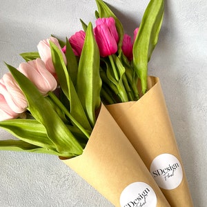 Op de afbeelding: Twee boeketten tulpen, &eacute;&eacute;n met lichtroze bloesems en de andere met levendige fuchsia bloemen. De groene bladeren en stelen zijn verpakt in bruine papieren kegels, elk met een witte sticker met "SDesign Floral".