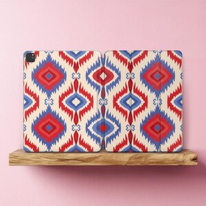 May include: A tablet case featuring a repeating geometric pattern in red, blue, and cream. The design consists of diamond-shaped motifs with jagged edges arranged in a symmetrical layout across the front and the folding cover of the device case.