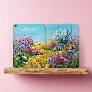 Könnte beinhalten: Eine Tablethülle mit einem Ölgemälde-Druck einer lebhaften Wildblumenwiese unter einem hellblauen Himmel. Das Design zeigt eine farbenfrohe Anordnung aus violetten, rosa, gelben und weißen Blumen mit deutlich sichtbaren Pinselstrichen.