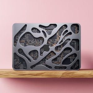 Può includere: Una custodia per laptop argentata con un design traforato unico che rivela i circuiti interni. La custodia presenta un logo Apple grigio scuro e poggia su una mensola di legno su sfondo rosa. Il design è moderno e ispirato alla tecnologia.