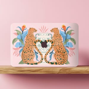 May include: A rectangular laptop case with a design of two cheetahs facing each other, either side of a vase with an apple-shaped design. The background is light pink with blue and orange floral accents. The cheetahs are orange with black spots.