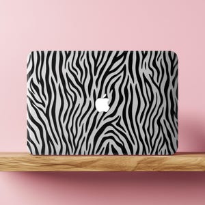 May include: A rectangular laptop skin featuring a high-contrast black and white zebra stripe pattern. The design covers the entire surface of the device, which displays a centered white Apple logo cutout, creating a bold and graphic visual effect.
