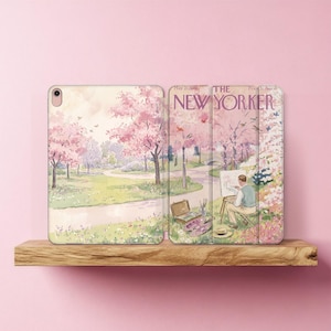 Puede incluir: Una funda protectora para tableta con una ilustración de un parque con cerezos en flor de color rosa. El diseño incluye el texto THE NEW YORKER y muestra a una persona pintando en un caballete en un campo con materiales de arte.