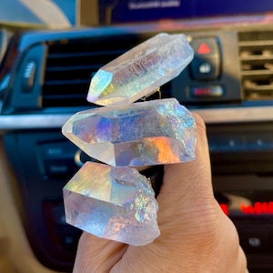 May include: Three iridescent clear quartz crystals stacked on top of each other. The crystals are pointed and have a rainbow sheen.