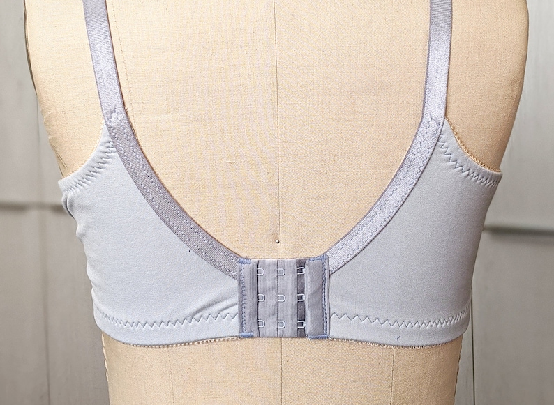 Może przedstawiać: Jasny szary biustonosz z regulowanymi ramiączkami i zapięciem na haftki z tyłu.