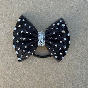 May include: A black hair bow made of mesh fabric, adorned with scattered silver rhinestones. The center of the bow features a band of sparkling rhinestones. A black elastic band is attached to the bow.